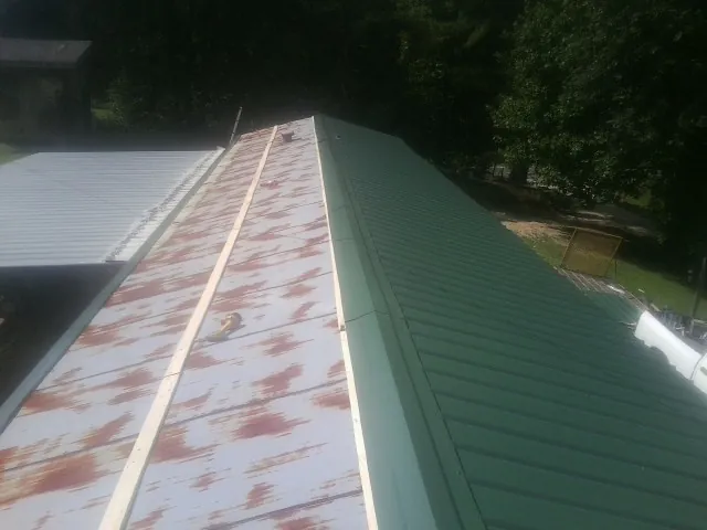 Old rusted panels beside newly installed green metal roofing — Wind Damage Roof Repair by Roofing Brothers in Graysville
