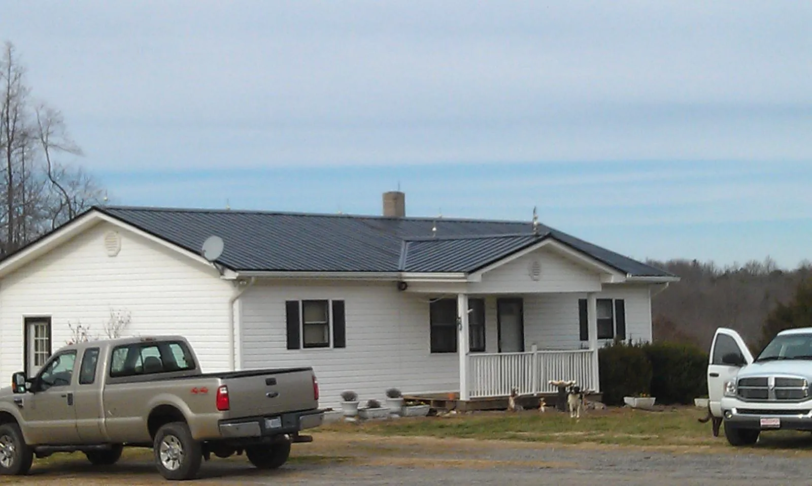 Finished dark metal roof on a white ranch home with work trucks parked in Graysville